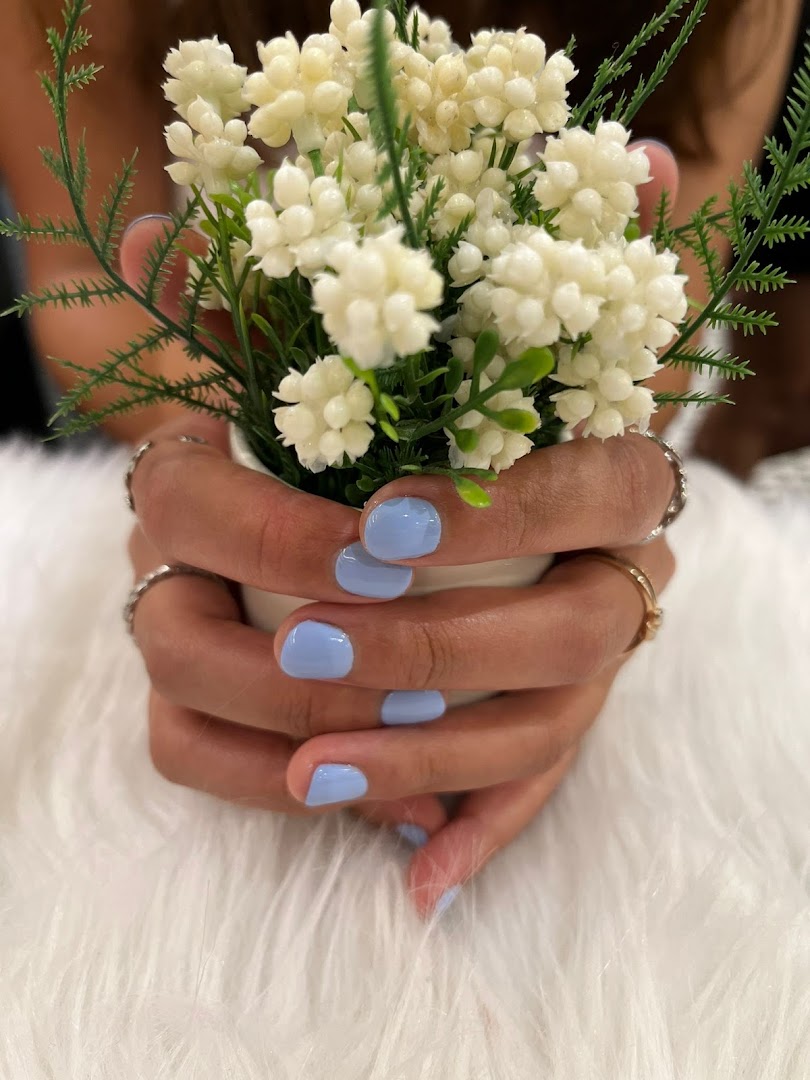 A close-up of hands with light blue manicured nails holding a small potted plant on a white furry surface.