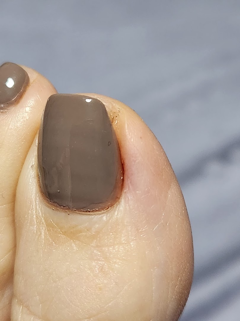 A close-up of a foot with a freshly painted toenail in a neutral shade.