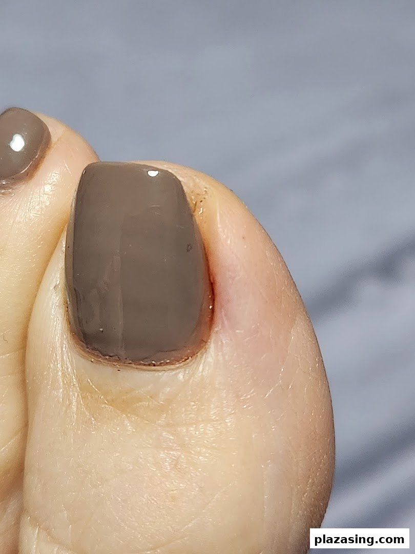 A close-up of a foot with a freshly painted toenail in a neutral shade.