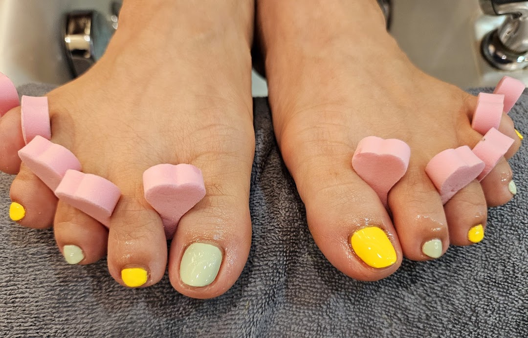 Close-up of feet with vibrant yellow and mint green toenail polish, using pink toe separators.