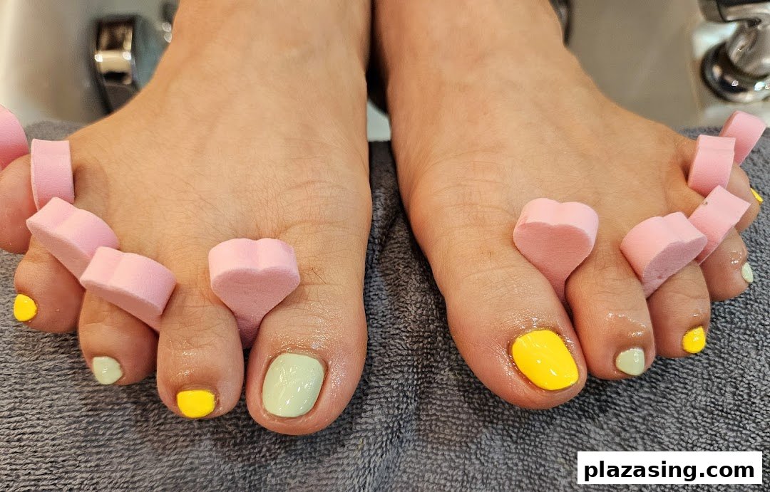Close-up of feet with vibrant yellow and mint green toenail polish, using pink toe separators.