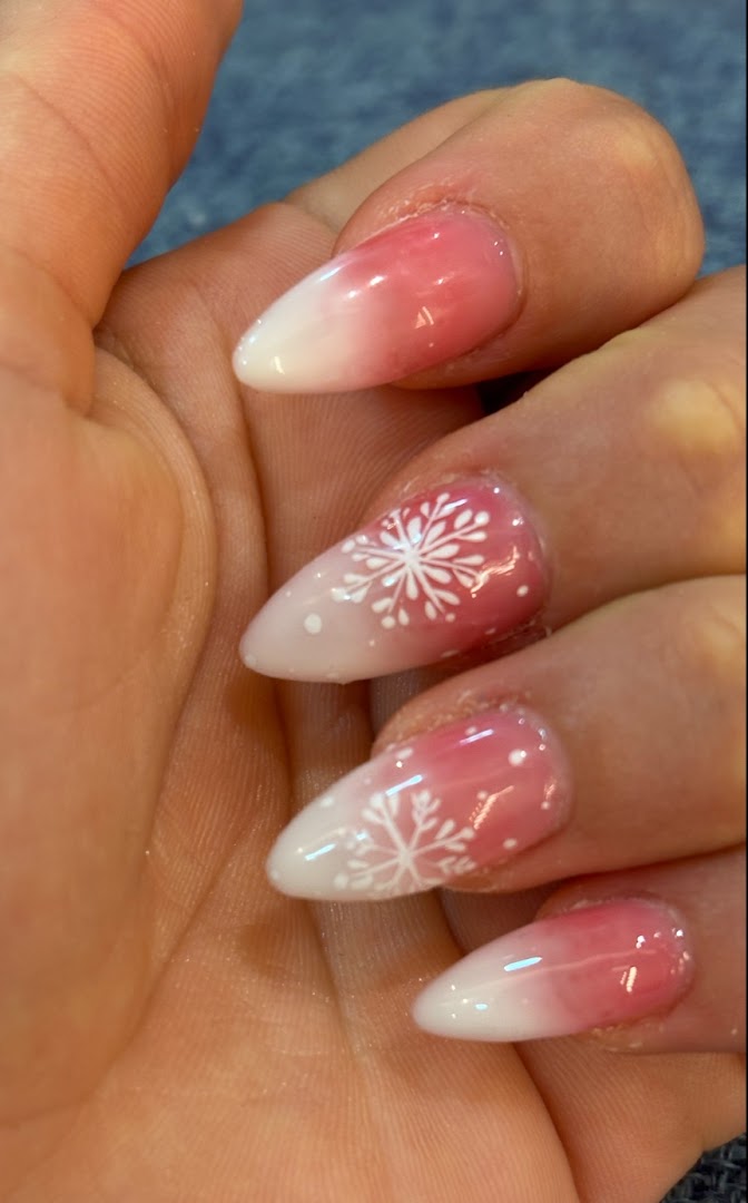 Close-up of a hand showcasing pink and white ombre nails with delicate snowflake designs.