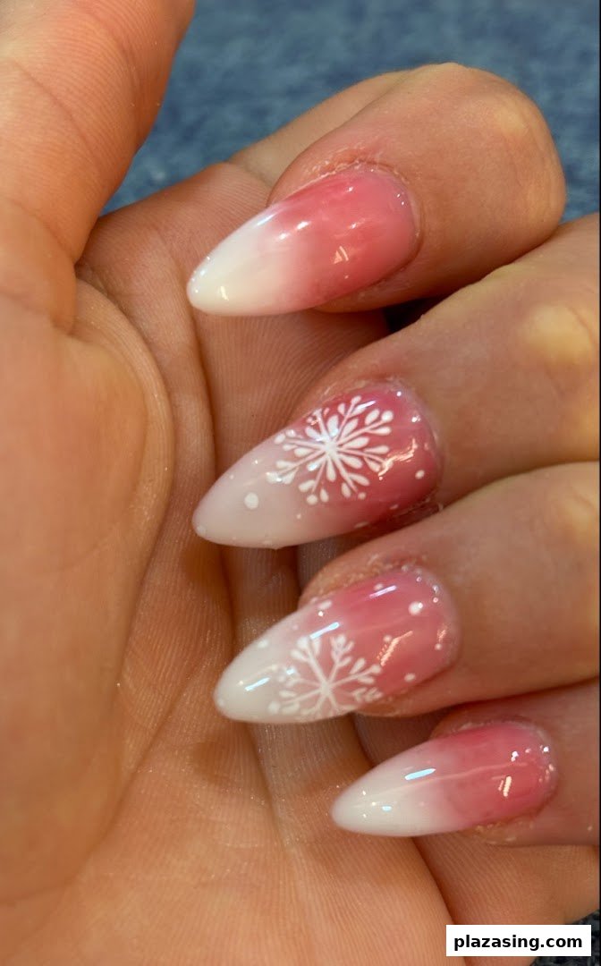 Close-up of a hand showcasing pink and white ombre nails with delicate snowflake designs.