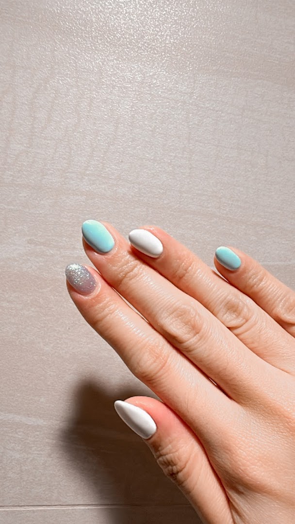 A hand showcasing a fresh manicure with white, light blue, and glitter nail polish.