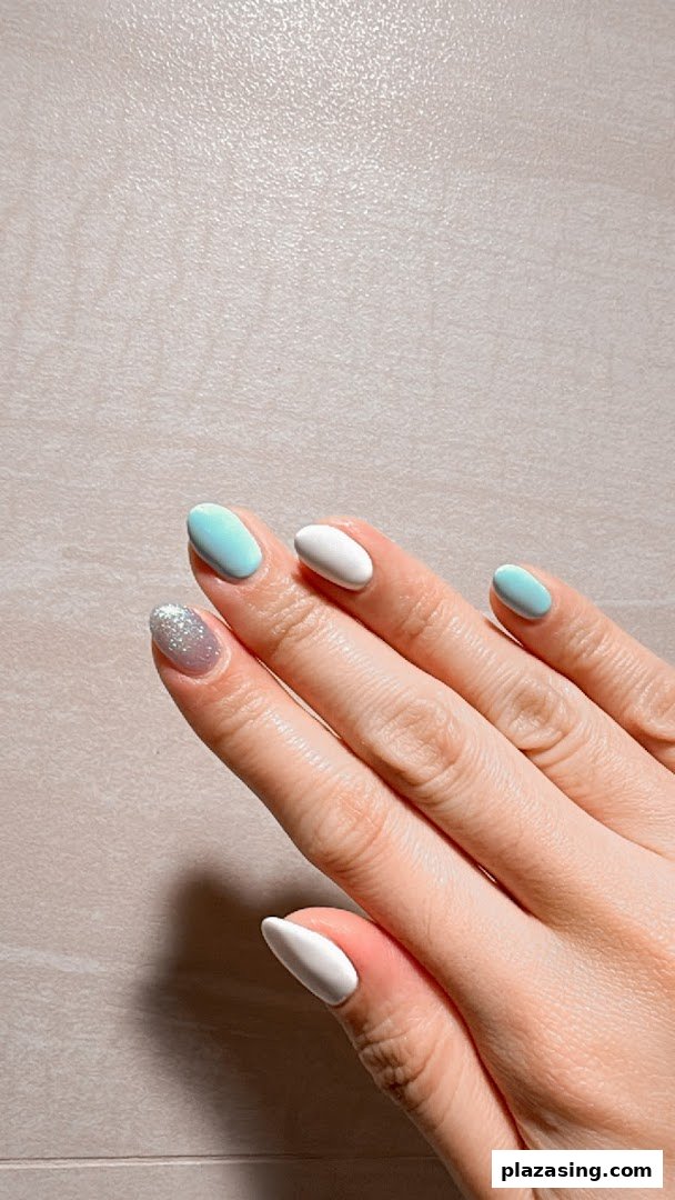 A hand showcasing a fresh manicure with white, light blue, and glitter nail polish.