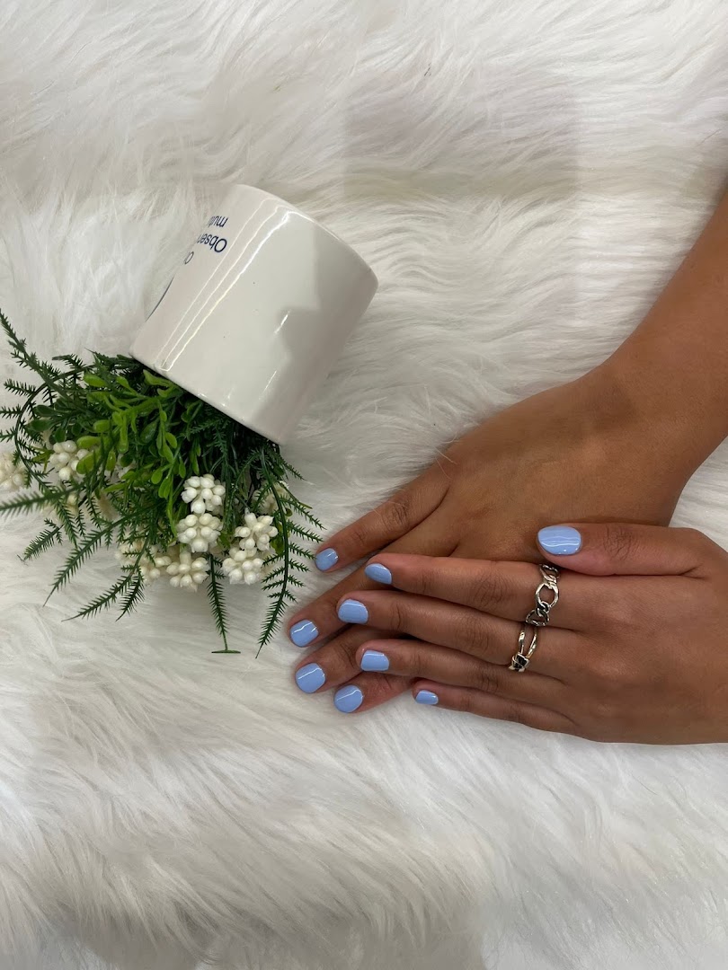 A person's hands with light blue nail polish and rings, next to a decorative plant on a white furry surface.