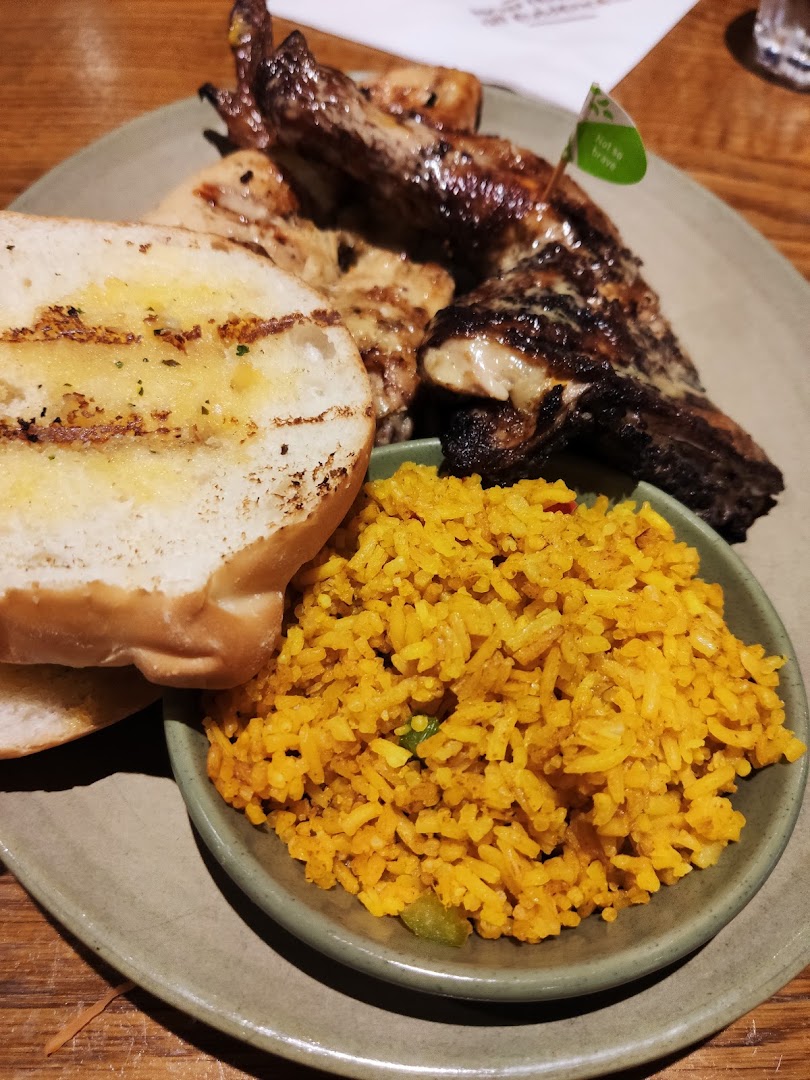 A close-up of Nando's flame-grilled PERi-PERi chicken with spicy rice and garlic bread.