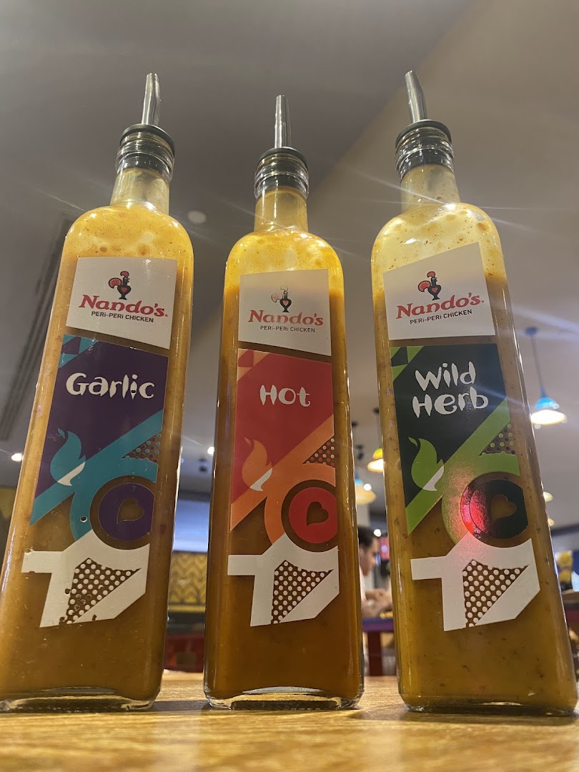 Three Nando's PERi-PERi sauce bottles (Garlic, Hot, Wild Herb) on a table.