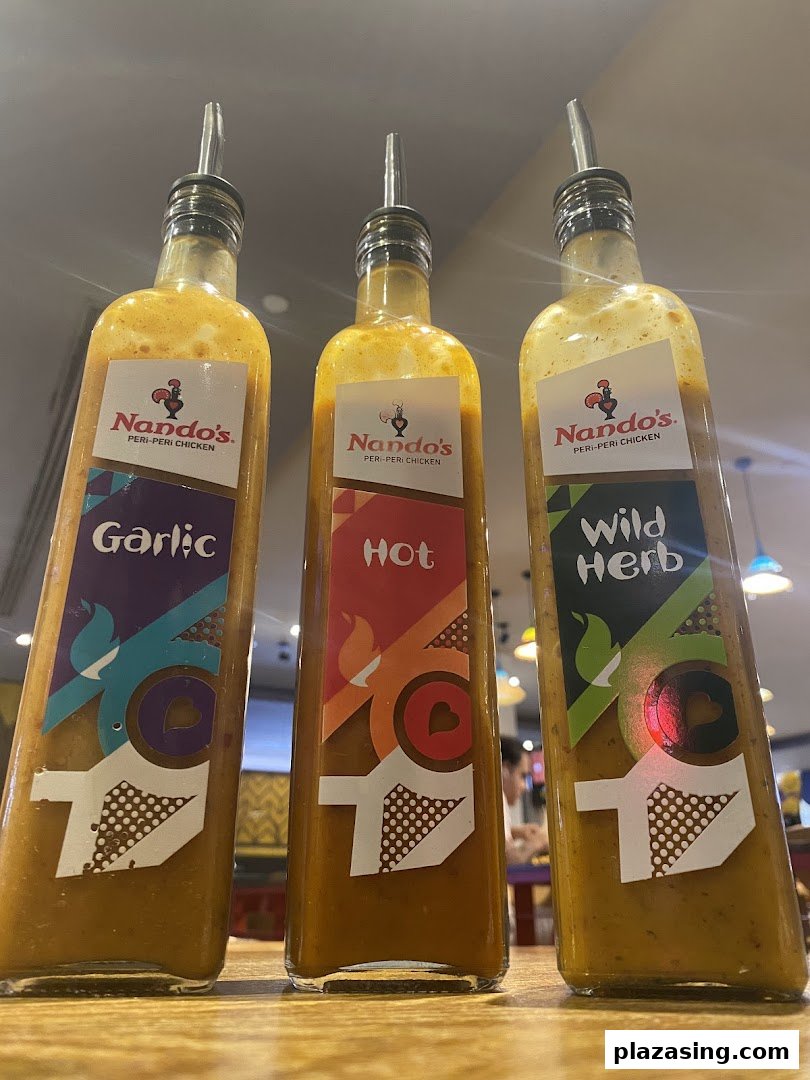 Three Nando's PERi-PERi sauce bottles (Garlic, Hot, Wild Herb) on a table.