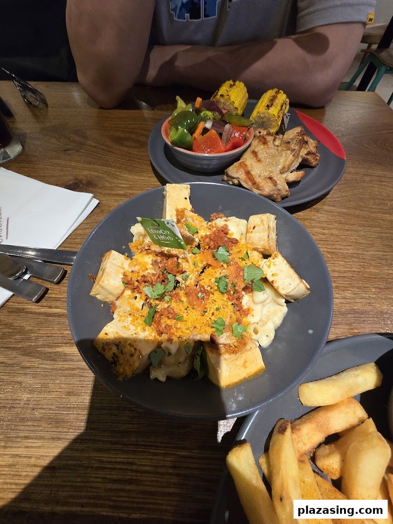 Plates of Nando's flame-grilled chicken, mac and cheese with tofu, vegetables, corn, and fries on a wooden table.