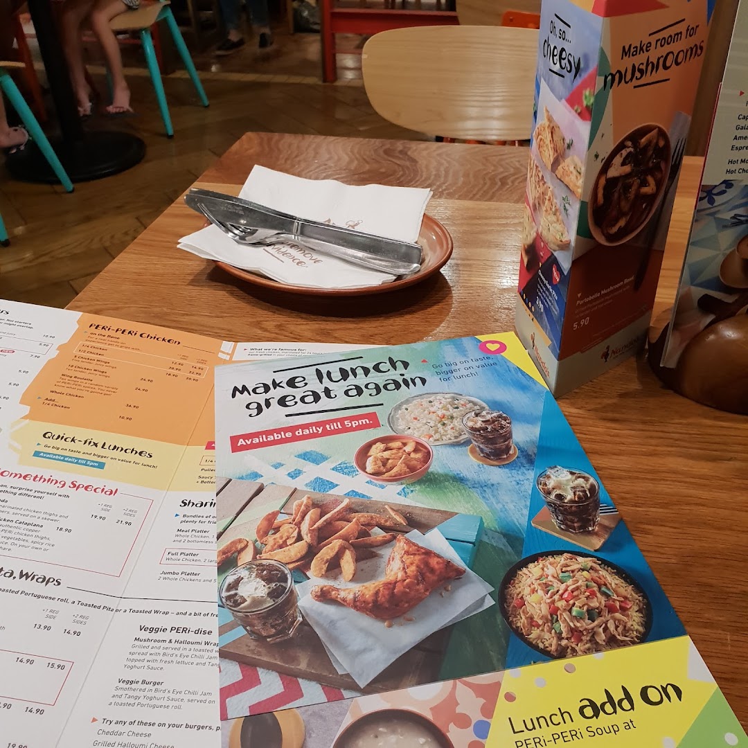 A table at Nando's with menus, cutlery, and promotional displays for PERi-PERi chicken and lunch specials.