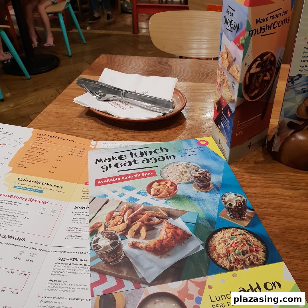 A table at Nando's with menus, cutlery, and promotional displays for PERi-PERi chicken and lunch specials.