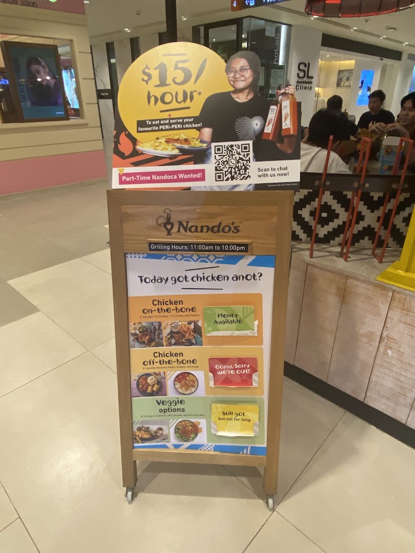 An A-frame sign at Nando's displaying chicken availability, grilling hours, and recruitment information.