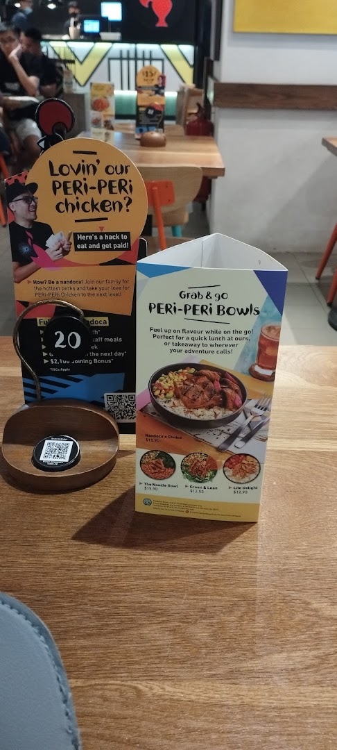 A Nando's restaurant table featuring promotional displays for PERi-PERi chicken bowls and staff recruitment.