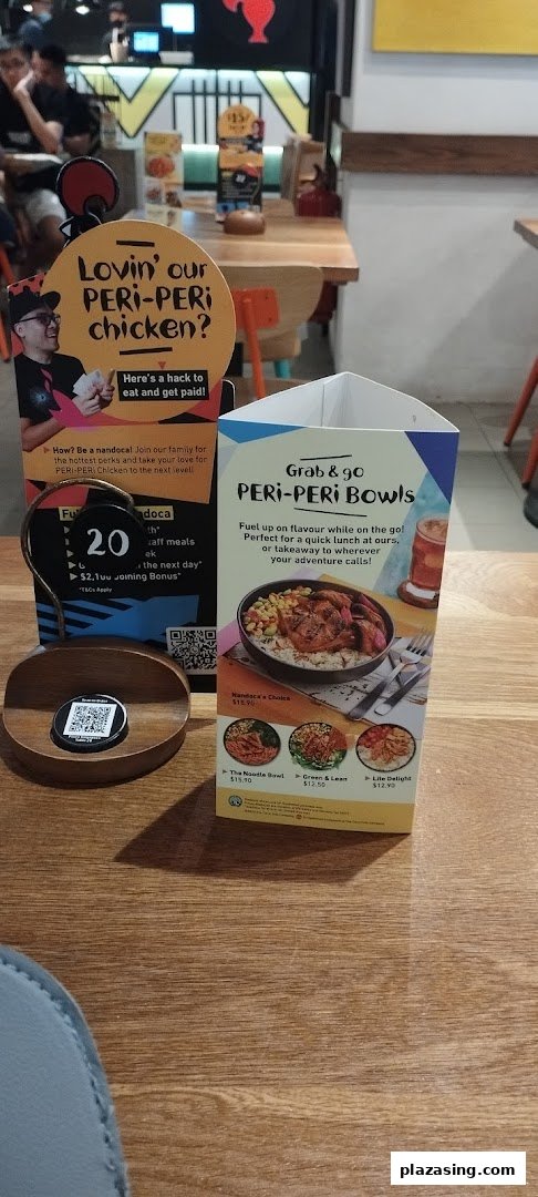 A Nando's restaurant table featuring promotional displays for PERi-PERi chicken bowls and staff recruitment.