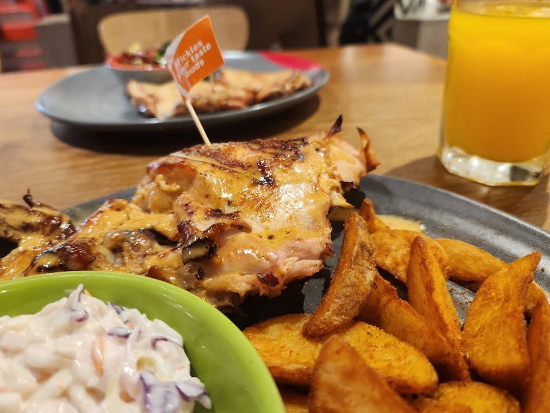 A close-up of Nando's flame-grilled PERi-PERi chicken, potato wedges, coleslaw, and a drink.