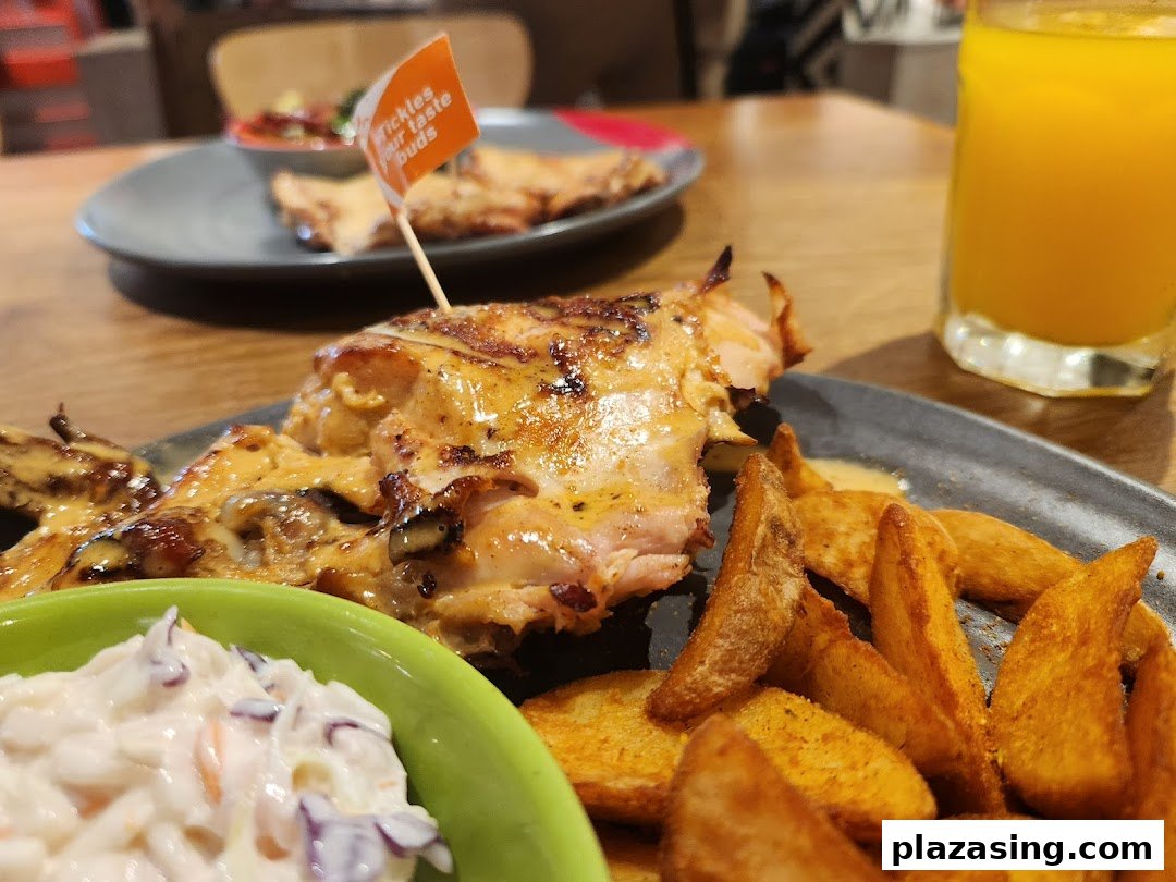 A close-up of Nando's flame-grilled PERi-PERi chicken, potato wedges, coleslaw, and a drink.