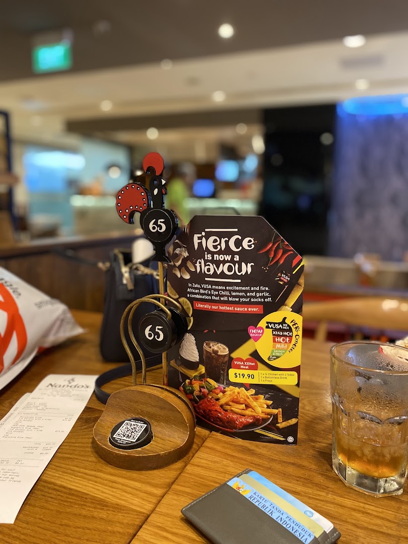 A Nando's table setting featuring a promotional stand for VUSA XXHot flavour and a receipt.