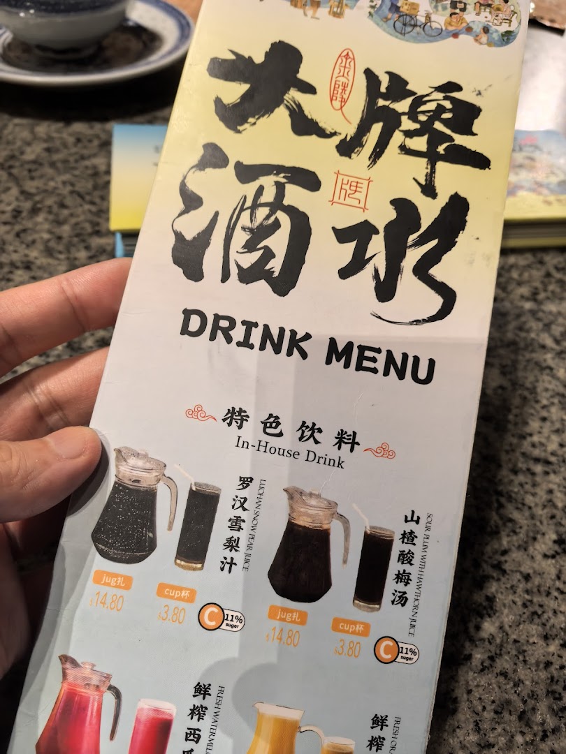 A hand holds open a drink menu displaying traditional Chinese beverages and prices.