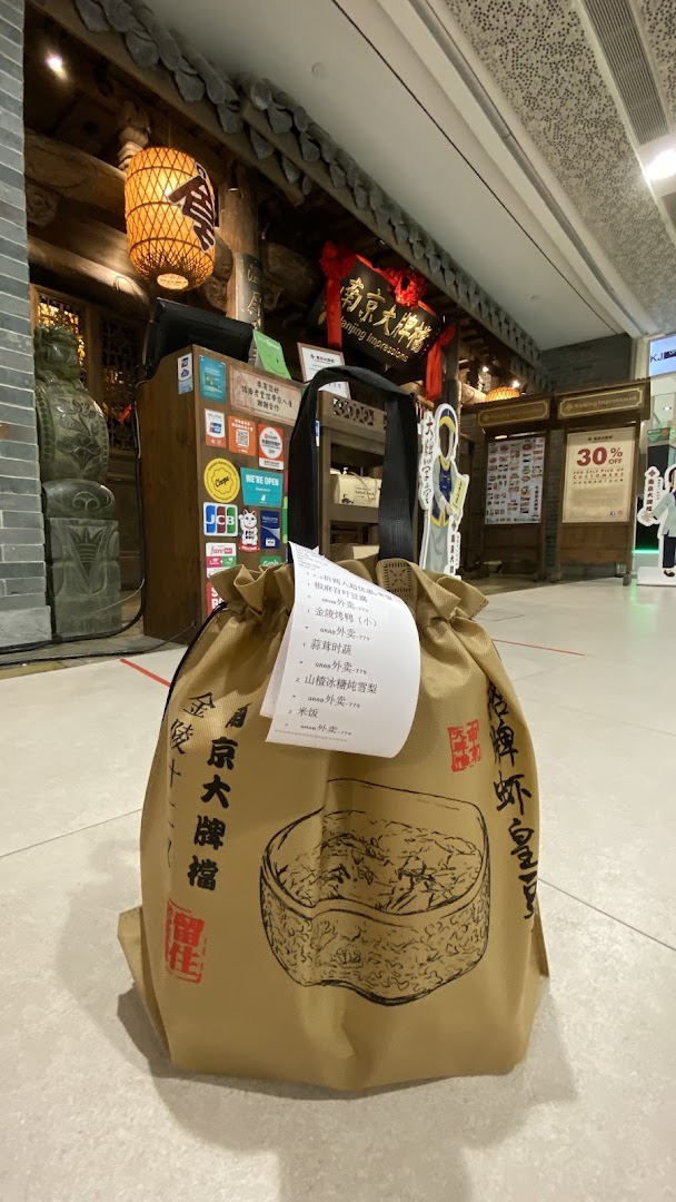 A takeaway bag from Nanjing Impressions restaurant stands before its traditional Chinese entrance.