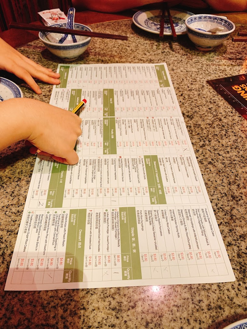 A person's hands are seen pointing at a detailed menu on a table in a restaurant setting.