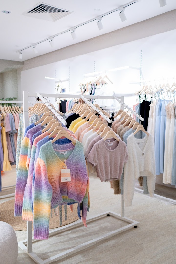 Brightly lit clothing store interior featuring colorful knitwear and pastel garments on display racks.