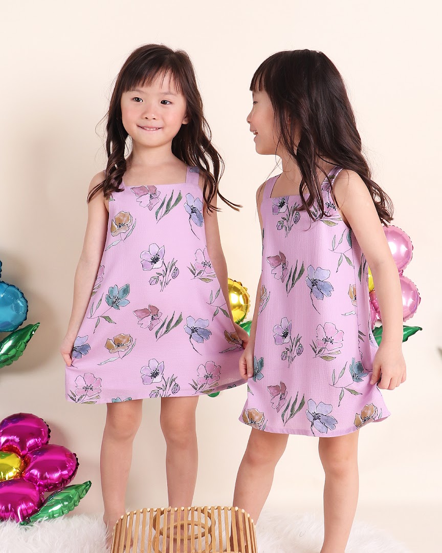 Two young girls in matching floral lavender dresses, surrounded by colorful balloons.