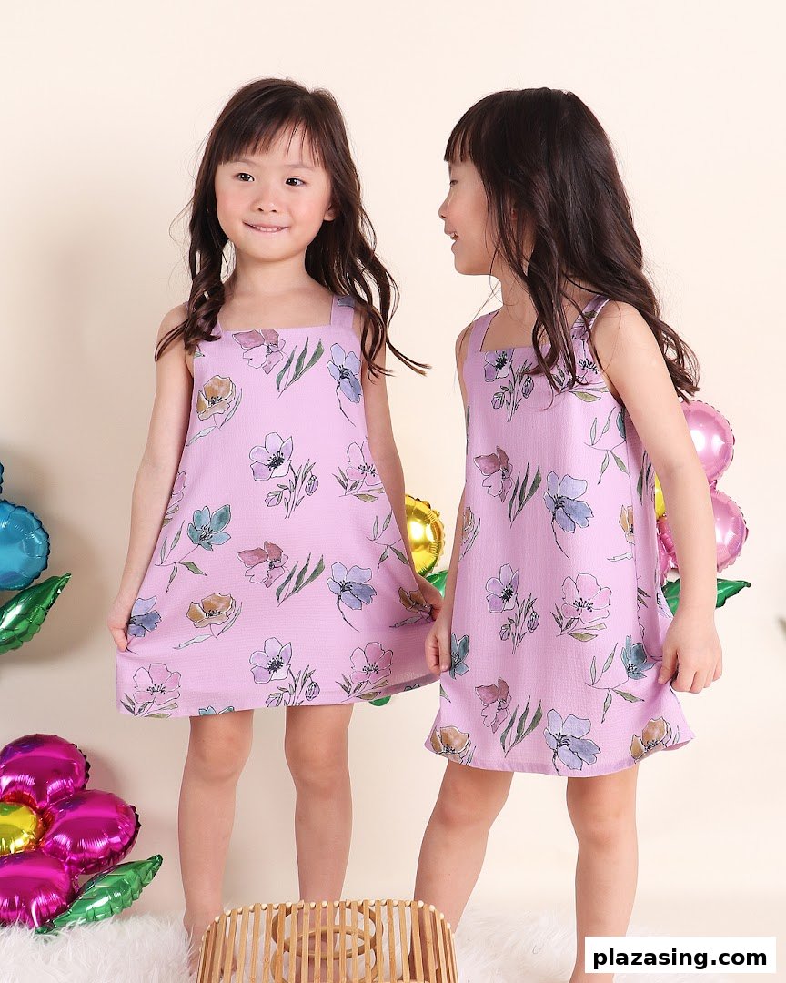 Two young girls in matching floral lavender dresses, surrounded by colorful balloons.