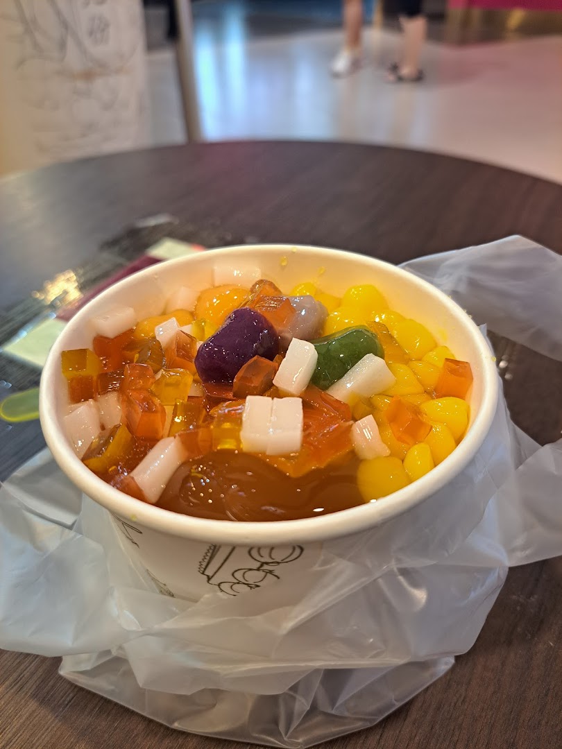 A vibrant bowl of Taiwanese dessert with colorful toppings, served in a cup on a table.