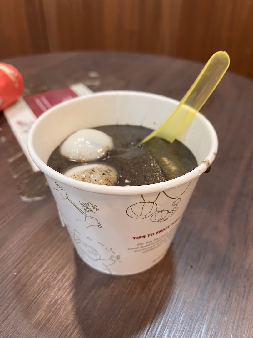 A cup of black sesame dessert with tangyuan and a yellow spoon on a wooden table.