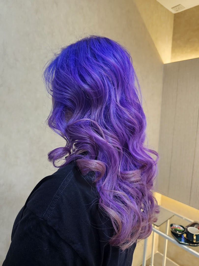 A person showcasing vibrant purple and lavender wavy hair, a result of a salon service.