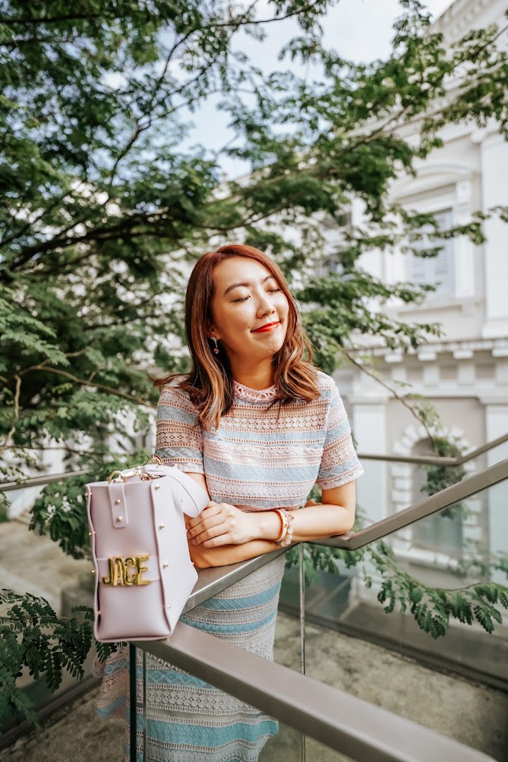 A woman with red hair and a patterned dress smiles outdoors, leaning on a railing.