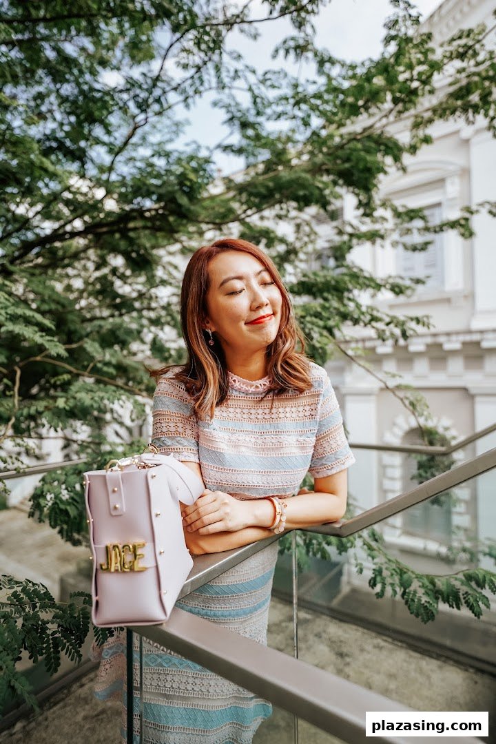 A woman with red hair and a patterned dress smiles outdoors, leaning on a railing.