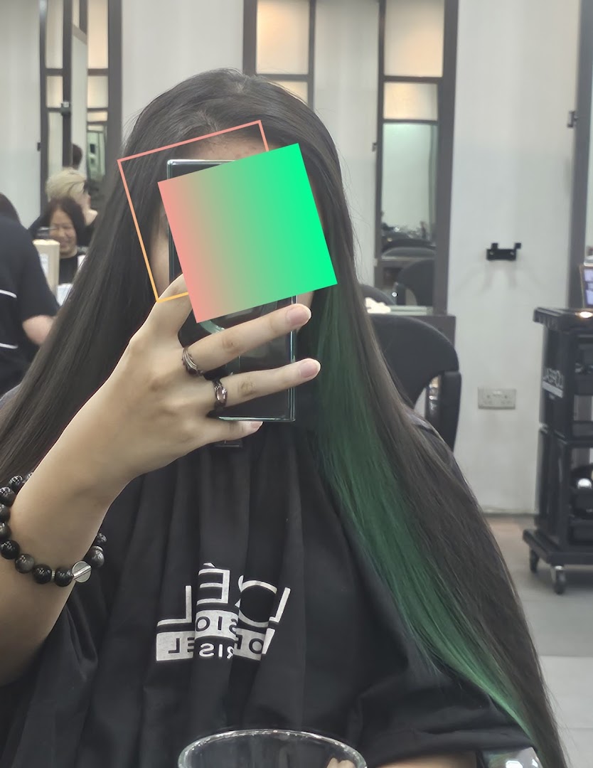 A person in a hair salon taking a selfie, showcasing long dark hair with vibrant green highlights.