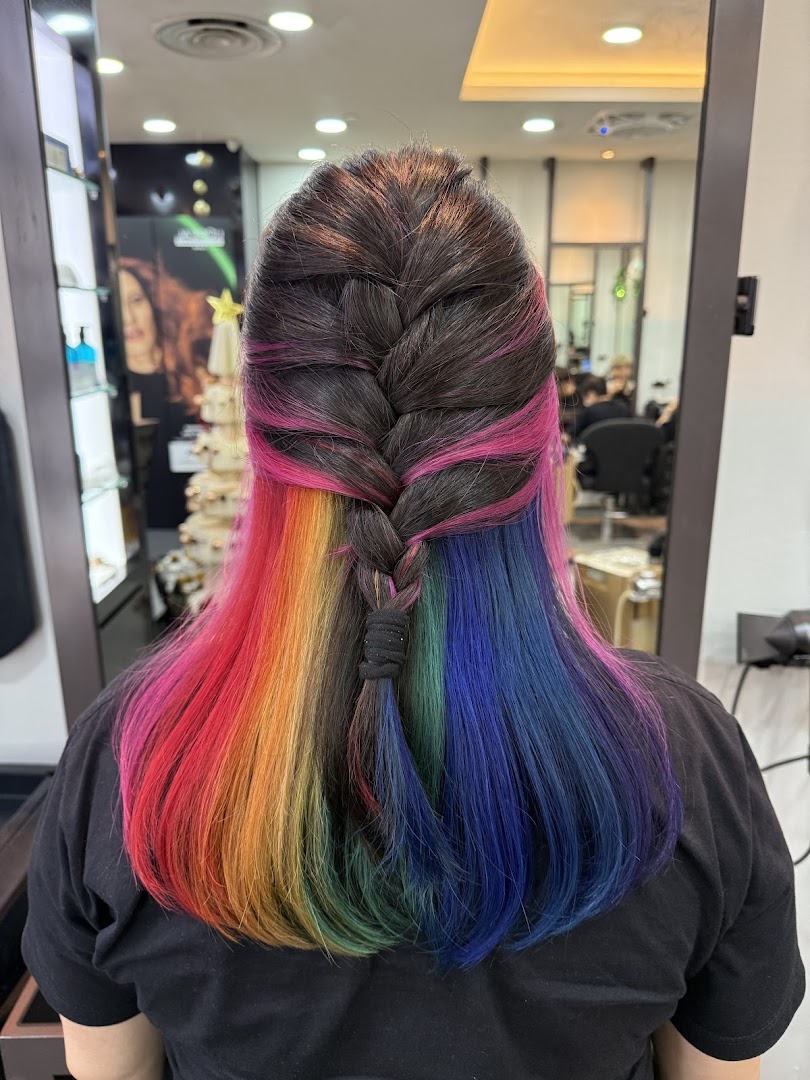 Rear view of a person with vibrant rainbow-colored hair styled in a half-braid at NK Hairworks.