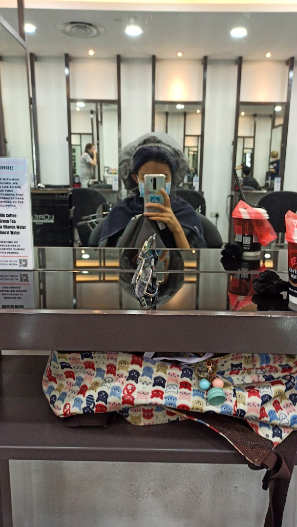 A customer wearing a hair cap and mask takes a mirror selfie inside NK Hairworks salon.