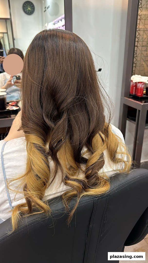 Rear view of a person showcasing brown hair with blonde highlights and styled curls in a salon.