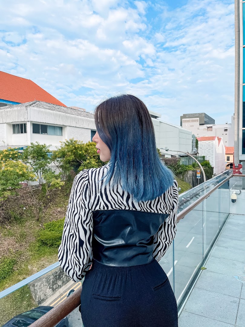 A person with vibrant blue hair stands on a bridge, looking out at the city skyline.