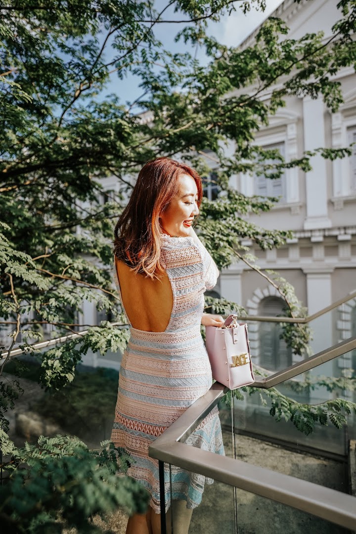 A woman with styled hair and a backless dress smiles while standing on an outdoor staircase.