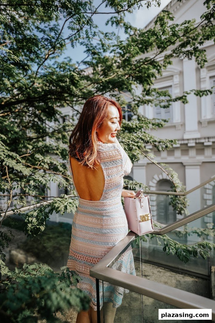 A woman with styled hair and a backless dress smiles while standing on an outdoor staircase.