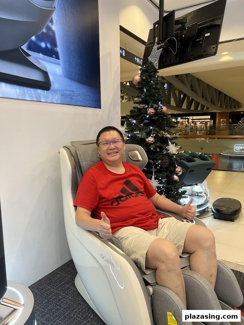 A man happily testing an OGAWA massage chair, giving thumbs up, with a Christmas tree nearby.