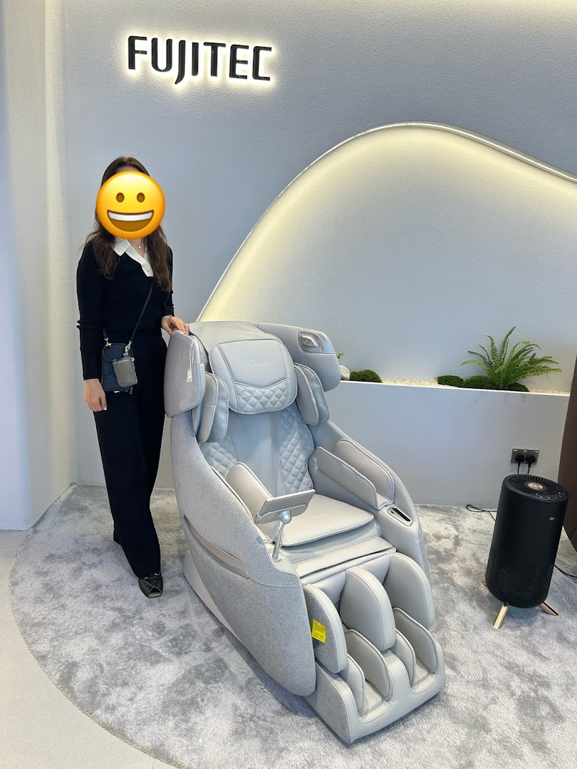A woman stands beside a sleek grey massage chair in a modern showroom, featuring the FUJITEC brand.