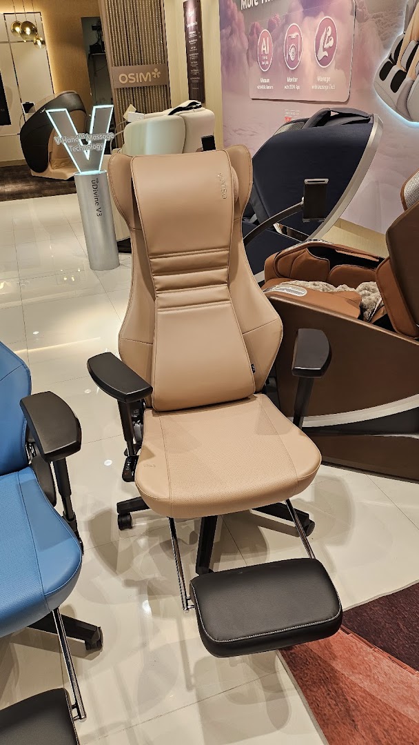 A beige massage chair with a footrest displayed in the OSIM shop, surrounded by other wellness products.