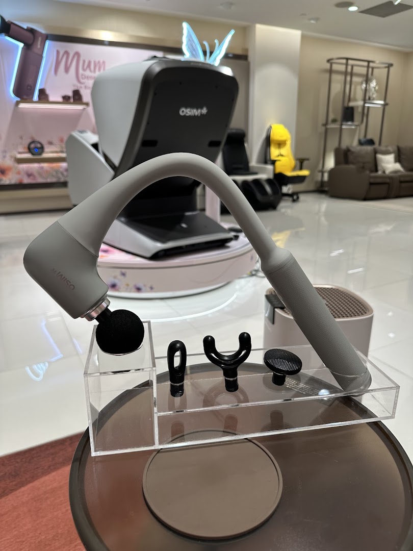 A massage gun with various attachments is displayed in the foreground, with OSIM massage chairs visible behind.