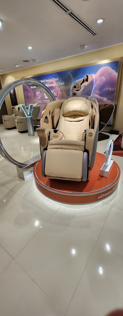 A modern beige massage chair displayed on a circular platform inside an OSIM store.