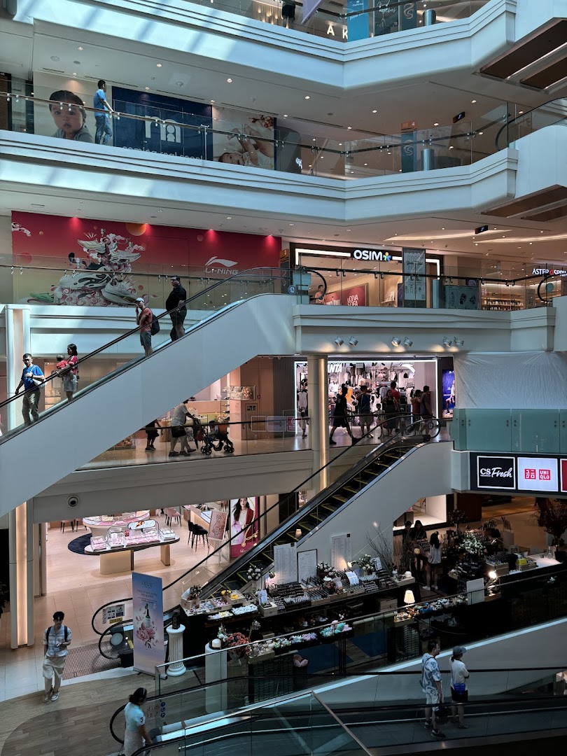 A bustling multi-level shopping mall interior with escalators and various retail stores, including OSIM.