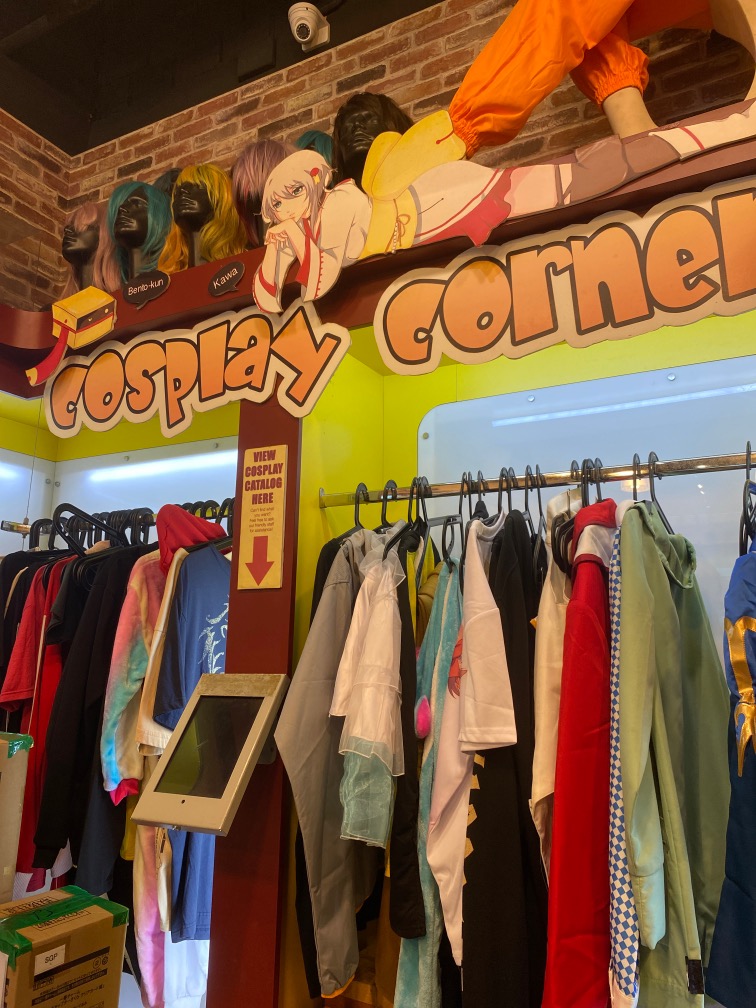 Interior view of Otaku House's cosplay corner featuring costumes, wigs, and anime decor.