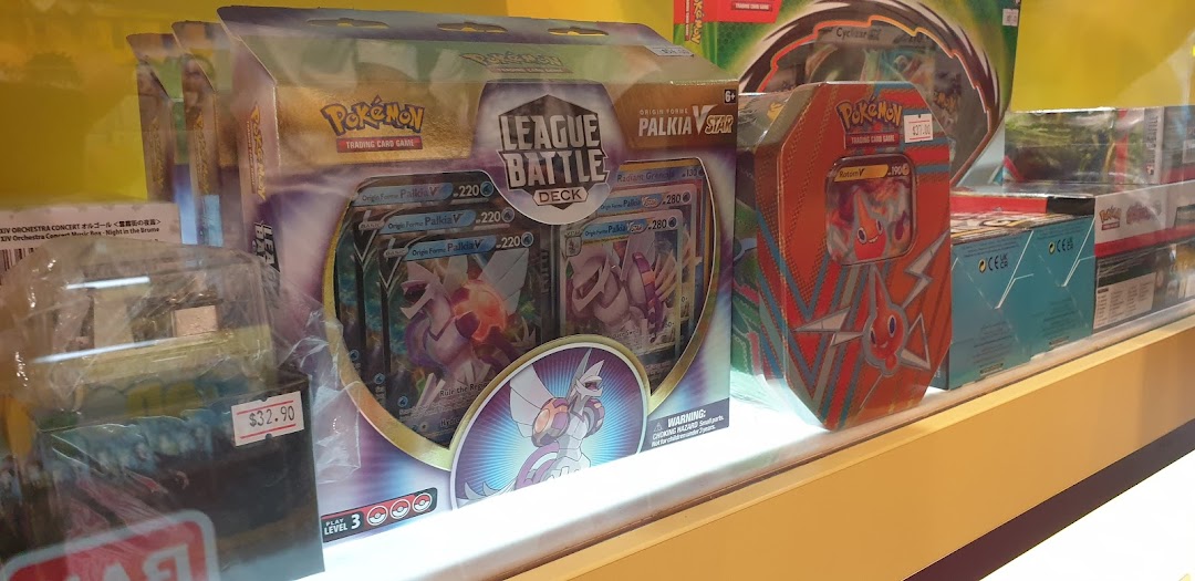A display case filled with various Pokémon Trading Card Game products, including League Battle Decks and tins.