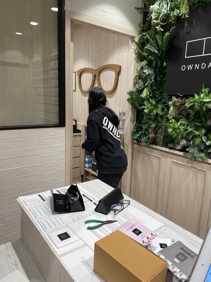 A staff member assists a customer at the service counter of OWNDAYS eyewear shop.