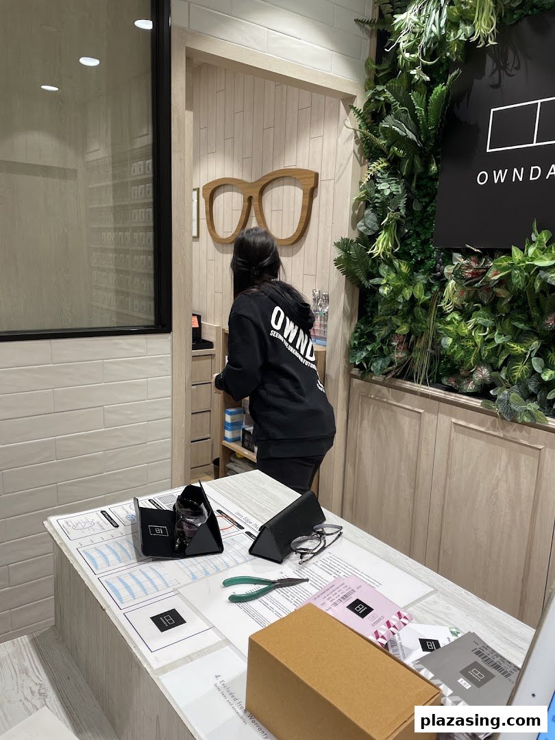 A staff member assists a customer at the service counter of OWNDAYS eyewear shop.